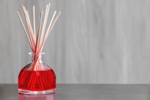 Air freshener, red fruits perfume diffuser shot with copy space on blurred wooden background. Air freshener, red fruits perfume diffuser and stems of reeds to spread a perfume slowly indoors. Object placed on gray table with blurred wooden background, horizontal shot photography.
